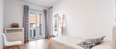 A bedroom with a bed, a desk, a chair, a wardrobe, and a window with curtains.