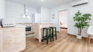 Cozinha moderna com armários brancos, uma ilha central, banquetas verdes e uma planta em vaso.