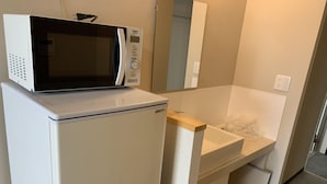 A compact kitchenette with a microwave on top of a refrigerator, a sink with a wooden countertop, and a small cabinet below. - Mr.KINJO in Kokusaidori (Naha)