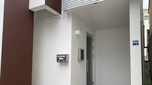 A narrow hallway with a door leading to a room, a mailbox, and a sign indicating the room number 7-6. - Mr.KINJO in Kokusaidori (Naha)