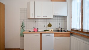 A compact kitchen with white cabinets, a dishwasher, and a window with sheer curtains. - Family-friendly Ortler vacation apartment.  (Taufers im M.)