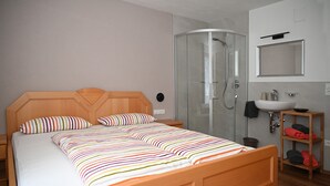 A bedroom with a wooden bed, striped bedding, a glass shower enclosure, a wooden nightstand, and a bedside table. - Family-friendly Ortler vacation apartment.  (Taufers im M.)