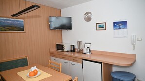 A compact kitchen with a microwave, coffee maker, and small refrigerator. A dining table with chairs is positioned in front of the counter. - Family-friendly Ortler vacation apartment.  (Taufers im M.)