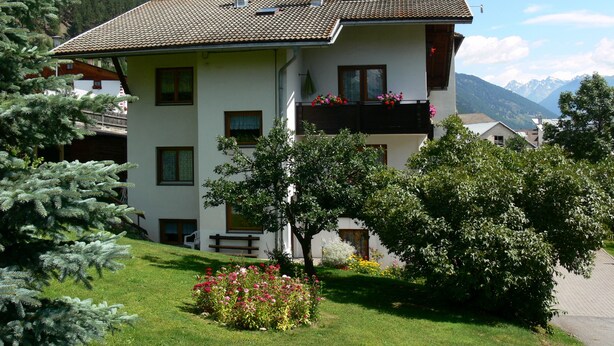 A multi-story building with a tiled roof, balconies with flower boxes, and a lush garden in front. - Family-friendly Ortler vacation apartment.  (Taufers im M.)