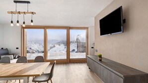 Un interno moderno con zona pranzo, televisore a parete e ampie finestre che offrono vista su una montagna innevata.