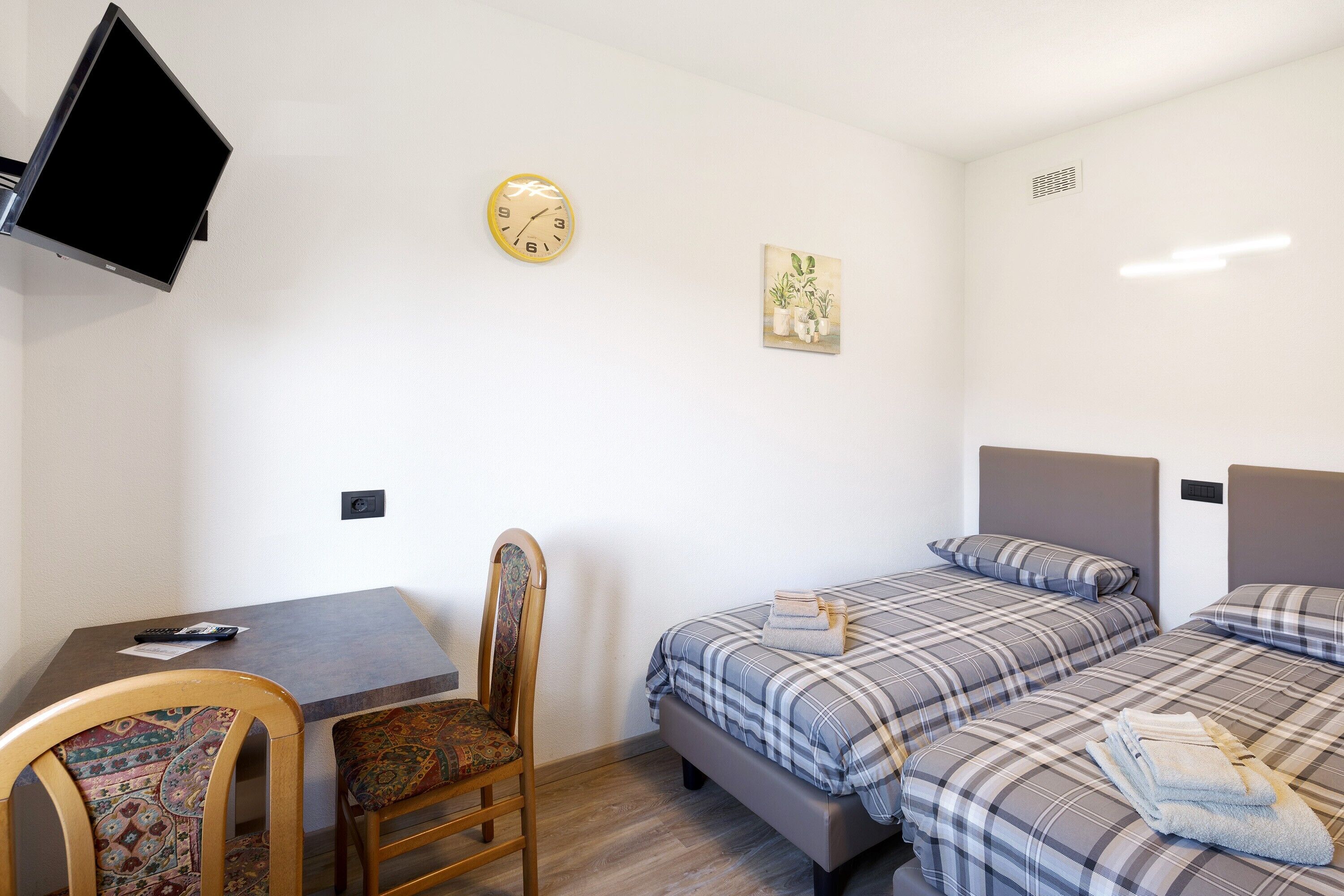 Une pièce comprenant un lit, une chaise, une table, une horloge et un téléviseur.