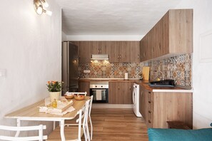 Une cuisine de taille réduite, dotée de meubles en bois, d’un pare-feu en carrelage et d’un coin repas avec une table et des chaises.