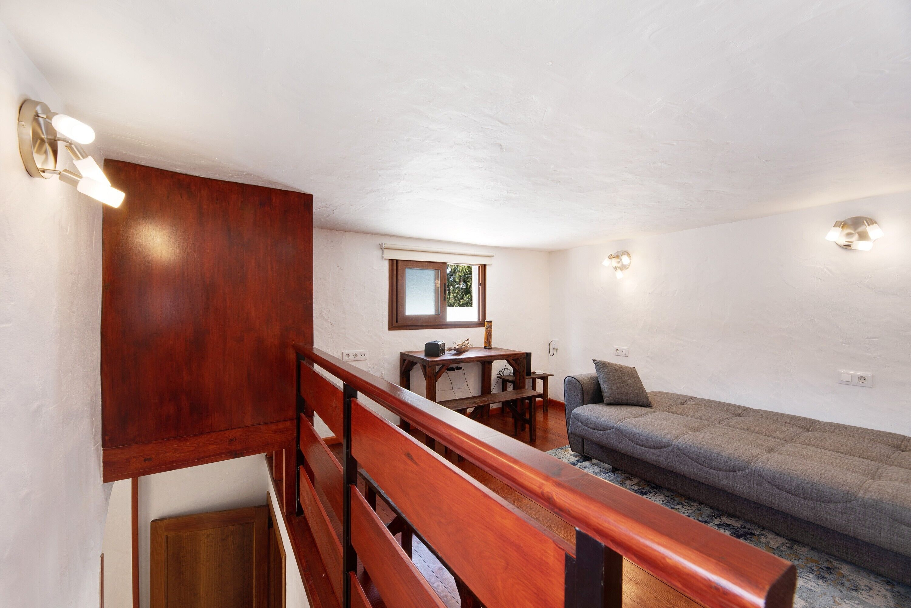 A room with a wooden bench, a sofa, a small table, and a window.