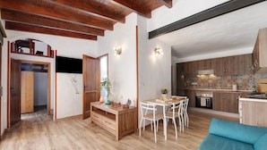 A spacious living area with a wooden floor, a dining table with chairs, a blue sofa, and a kitchen with wooden cabinets and a tiled backsplash. - Holiday Apartment "Casita Ana" with Mountain View & Private Terrace (El Paso)