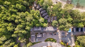 An aerial view of a resort with multiple buildings surrounded by dense forest, a parking area, and a beach. - Steps to Terrace Beach - Cozy Pet-Friendly Loft ⎮ Blue Heron (Ucluelet)