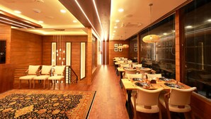 A modern restaurant with wooden paneling, a long dining area with tables and chairs, and a patterned rug. - Wooden ECR Sea Resort (Marakkanam)