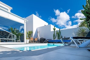 A pool area with lounge chairs, a table, and potted plants.