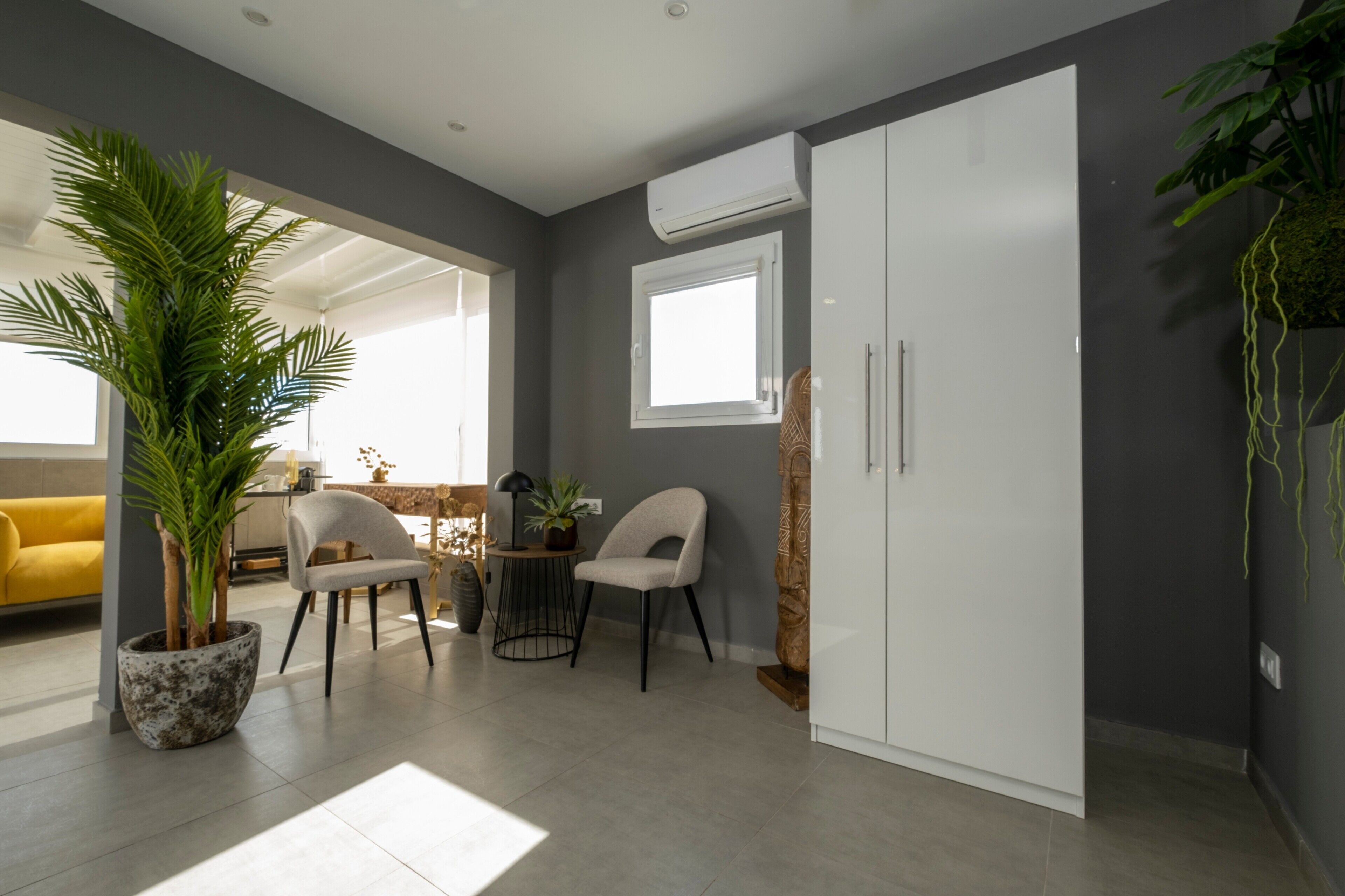 Una sala de estar moderna con una planta grande en maceta, dos sillones, una mesita y un armario blanco.