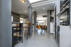 A modern kitchen with a dining area, a staircase, and a view to another room.