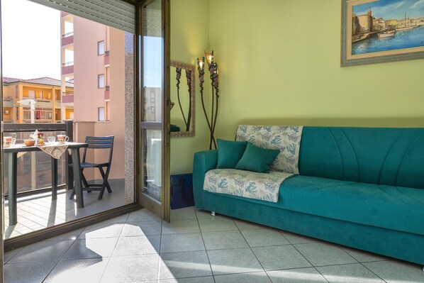 A balcony with a table and chairs, a teal sofa, a painting, and a mirror.