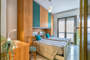 A bedroom with a bed, a desk, a chair, and a potted plant.