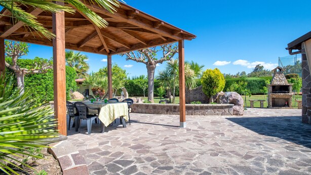 Eine überdachte Terrasse mit Steinböden, einer Holzpergola und einem Grillbereich aus Stein.