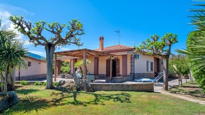 Ein Haus mit überdachter Terrasse, Steinmauern und einem Schwimmbad.
