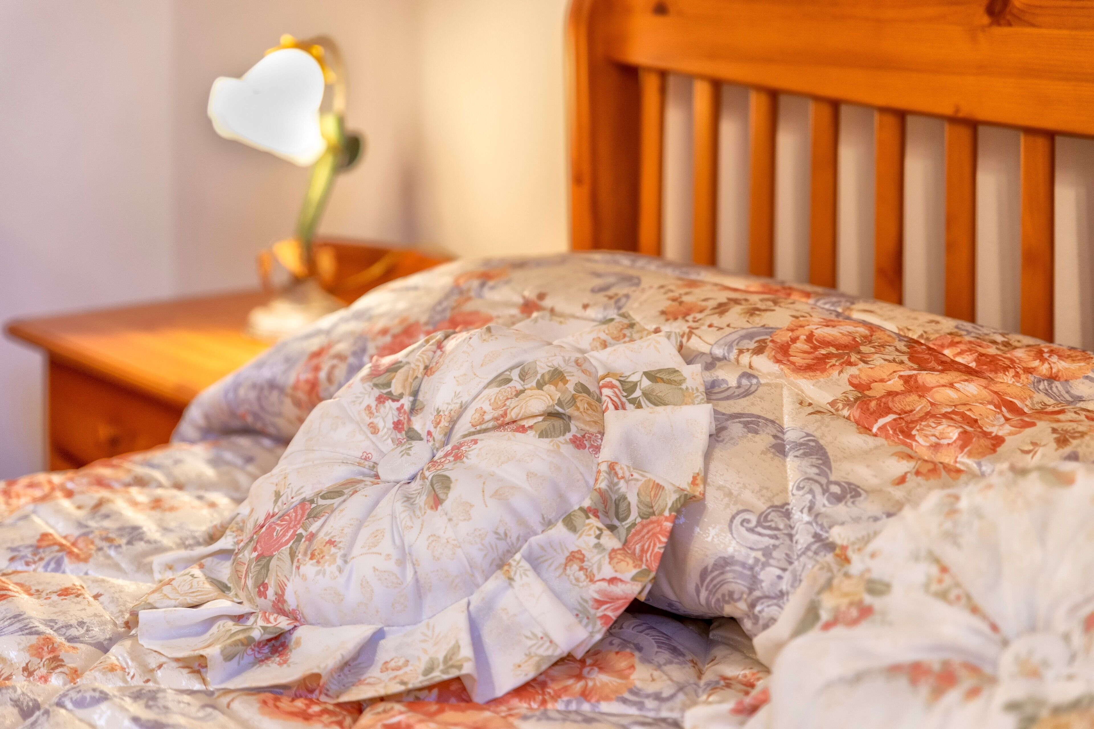 A bed with floral bedding, a wooden headboard, and a bedside table with a lamp.