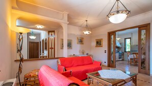 Ein Wohnzimmer mit einem roten Sofa, einem Glastisch und einem Essbereich, der durch einen offenen Durchgang sichtbar ist.