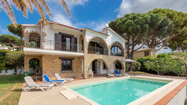 Ein zweistöckiges Haus mit Swimmingpool, Steinbögen und einem Balkon.