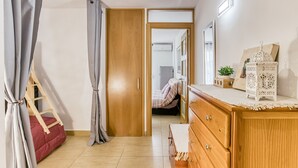 Een slaapkamer met een houten dressoir, een bed met een rode deken, een houten ladder en een deur die naar een andere kamer leidt.