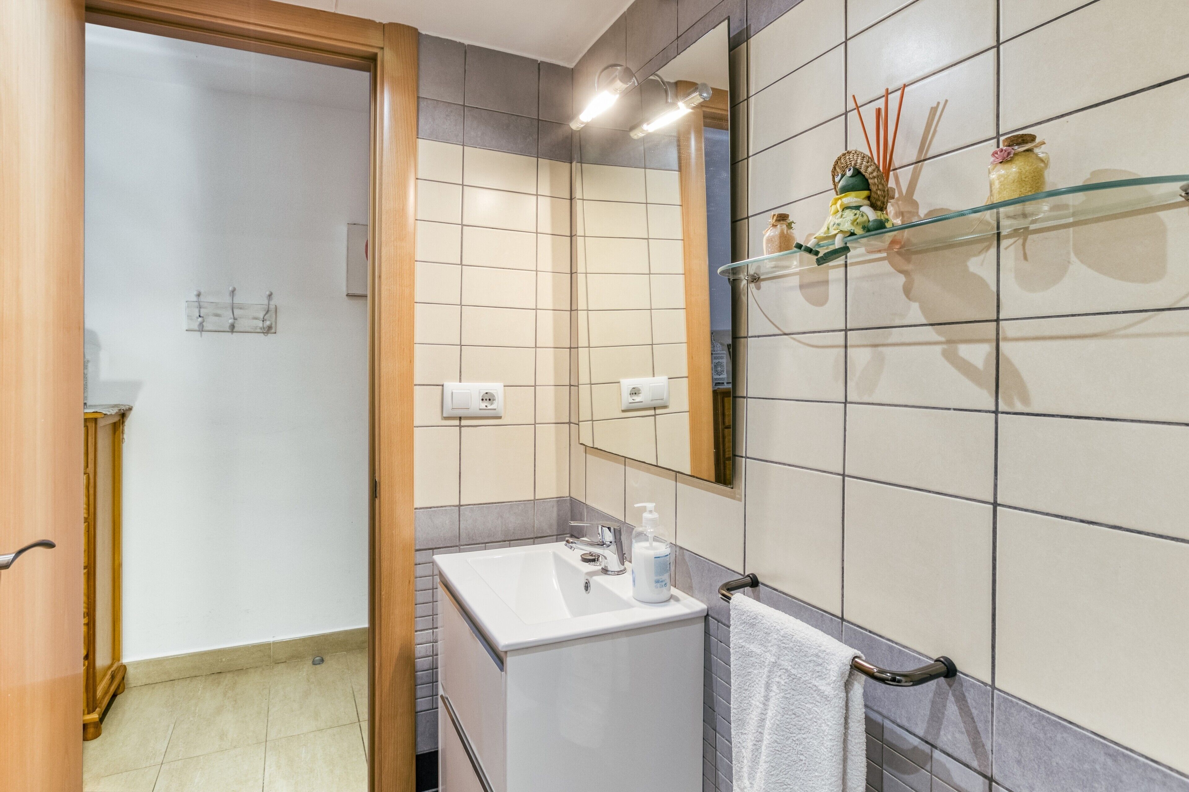 Une salle de bain avec un lavabo blanc, un miroir, un porte-serviettes et une étagère contenant des articles de toilette.