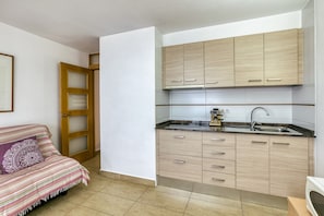 A compact kitchen with light wood cabinets, a stainless steel sink, and a striped sofa with a decorative pillow.
