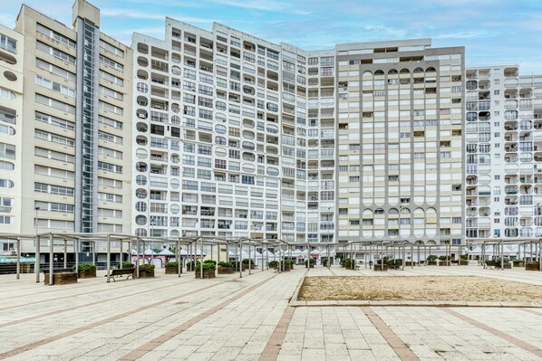 Un moderno edificio de apartamentos con varios balcones, un patio central con bancos y un corredor cubierto.