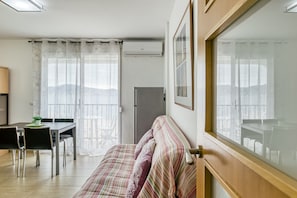 A room with a bed, a dining table with chairs, an air conditioning unit, and a window with curtains.