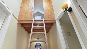 A loft bedroom with a wooden ladder, a skylight, and a wall-mounted lamp.