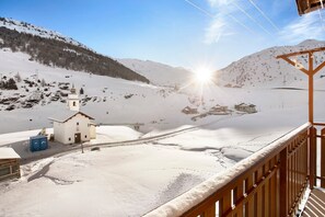 Paisaje nevado de montaña con un edificio pequeño, una valla de madera y cielo despejado.