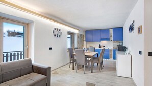 A modern kitchen with blue cabinets, a dining area with a table and chairs, and a grey sofa. - Apartment 'Presot' with Mountain View, Shared Garden & Wi-Fi (Livigno)