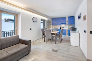 A modern kitchen with blue cabinets, a dining area with a table and chairs, and a grey sofa.