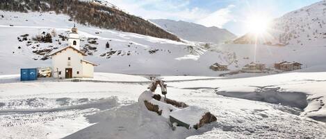 Un paysage enneigé avec un petit bâtiment, qui pourrait être une chapelle, et un bonhomme de neige.