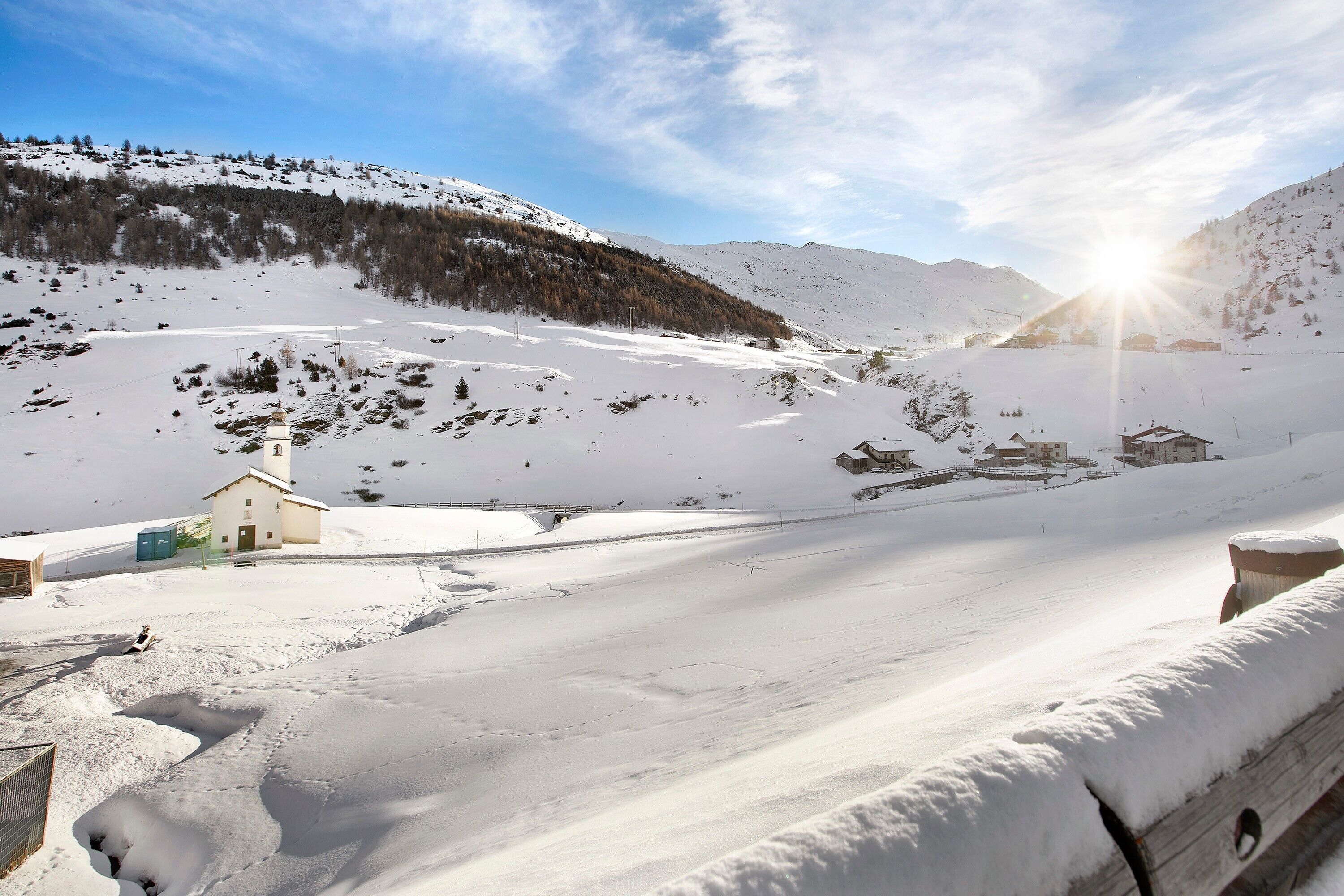 Paisaje nevado con un edificio pequeño, probablemente una cabaña, y una pista de esquí al fondo.