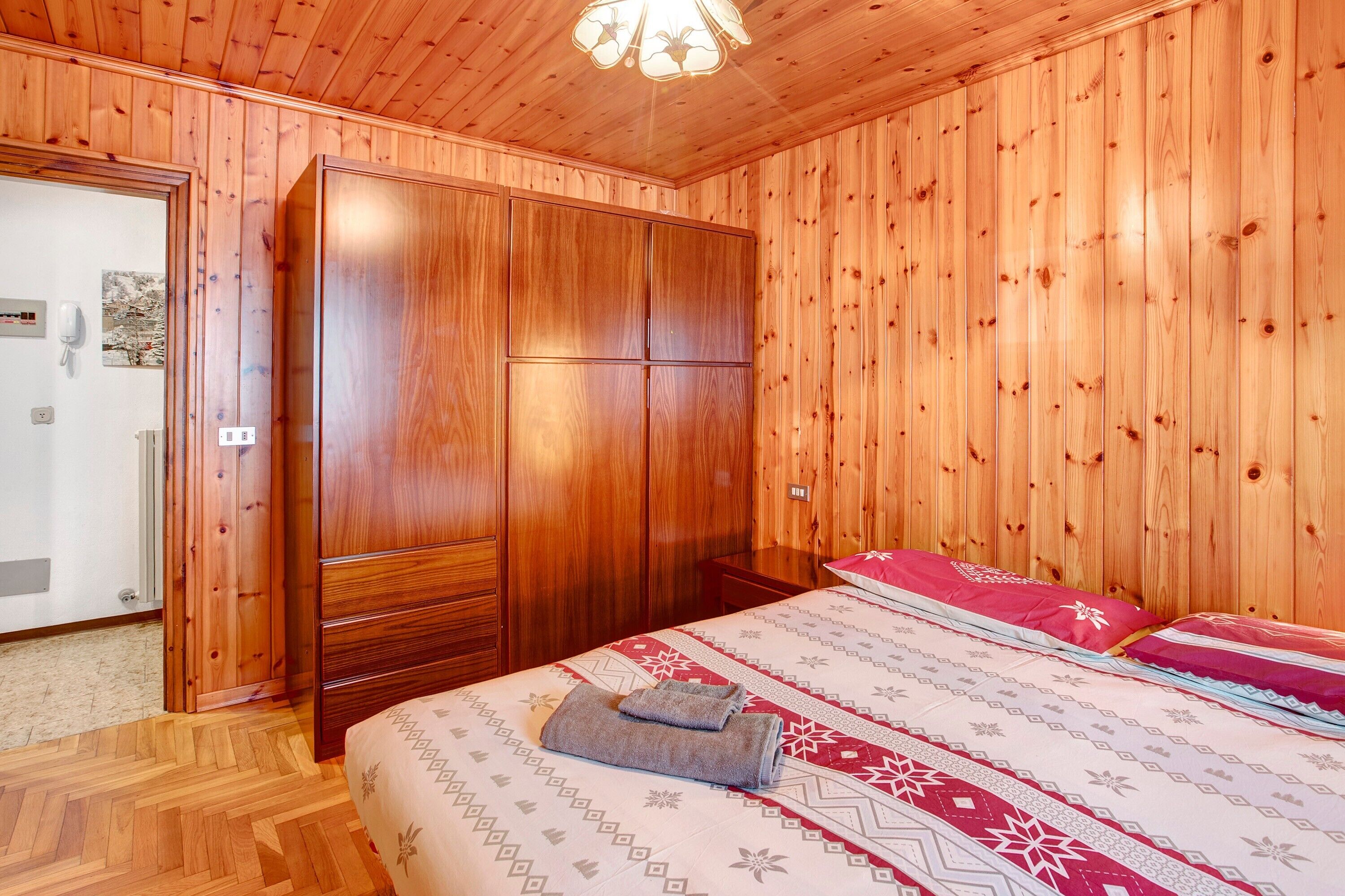 Une pièce aux murs lambrés, comprenant un lit, une armoire et une porte donnant sur une salle de bain.