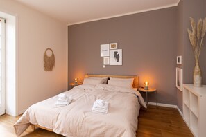 Cama arrumada com toalhas dobradas, uma obra de arte na parede e duas luminárias de cabeceira.