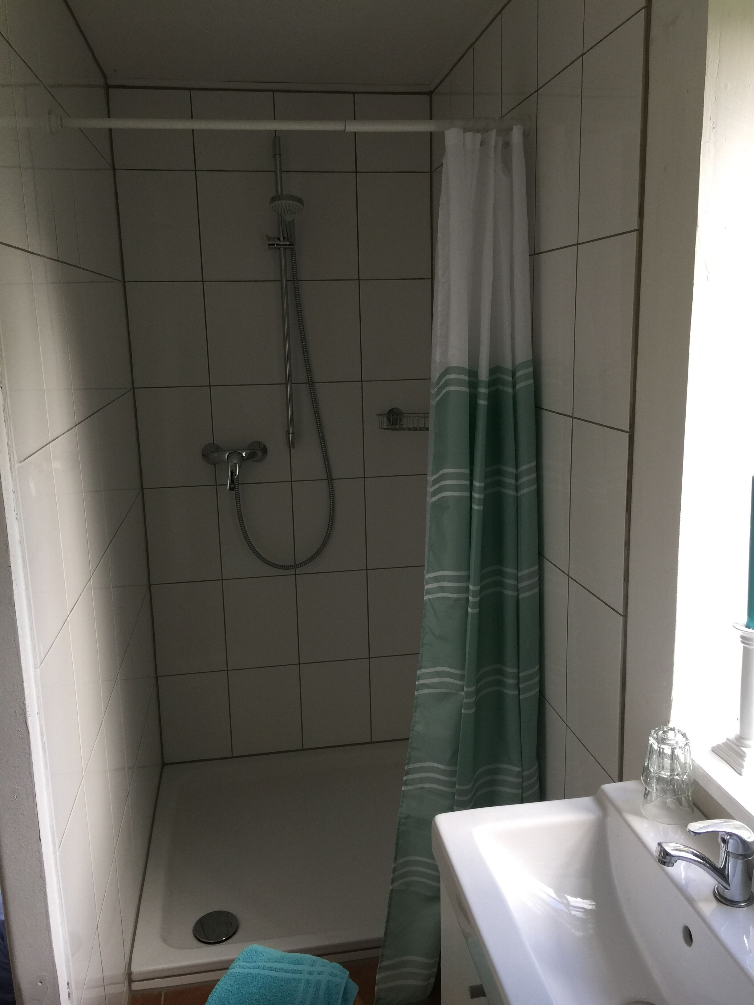 Ein kleiner Duschbereich mit gefliesten Wänden, einer Duschbrause und einem Duschvorhang.