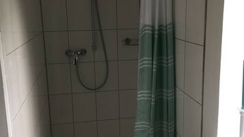 Ein kleiner Duschbereich mit gefliesten Wänden, einer Duschbrause und einem Duschvorhang.