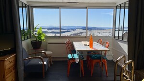A cozy room with a dining table, chairs, a potted plant, and a view of snowy mountains.