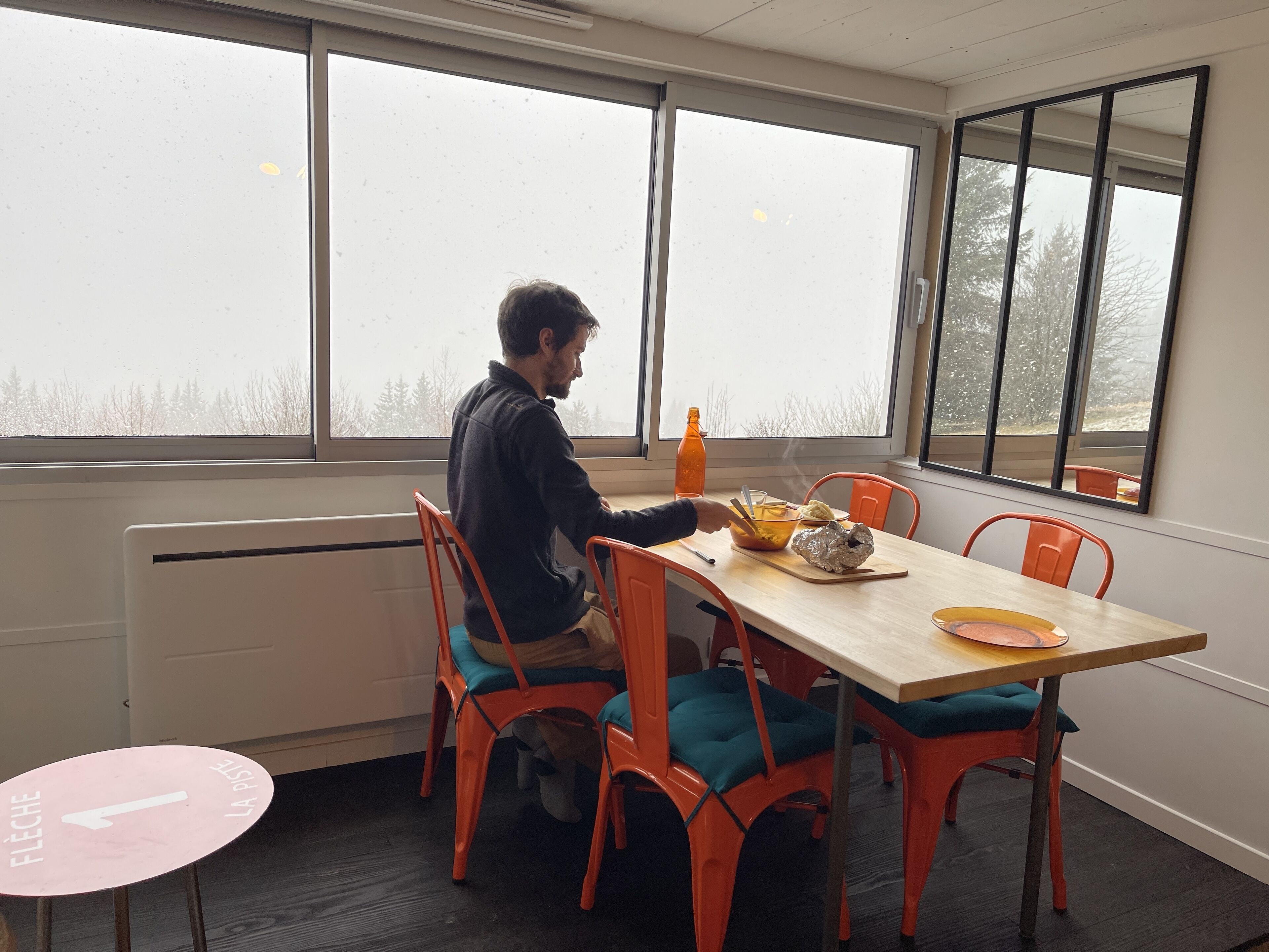 A dining area with a table and chairs, a window with a view of trees, and a radiator.