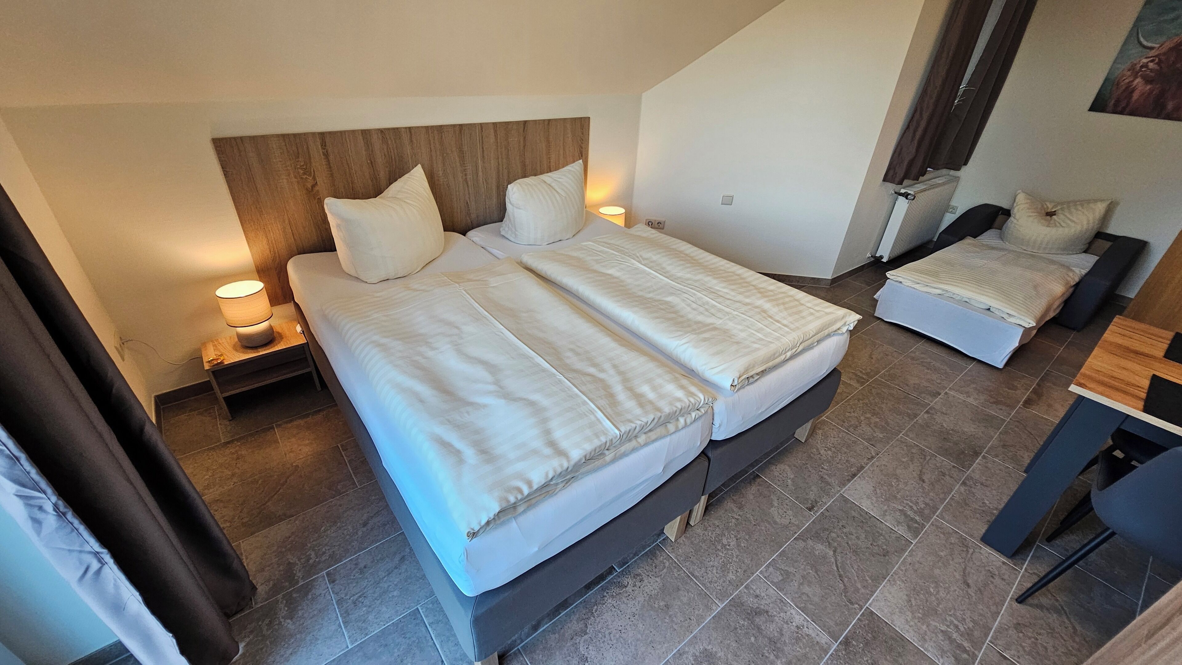 Ein Hotelzimmer mit zwei Betten, einem hölzernen Kopfteil, einem kleinen Schreibtisch und einer Heizung.