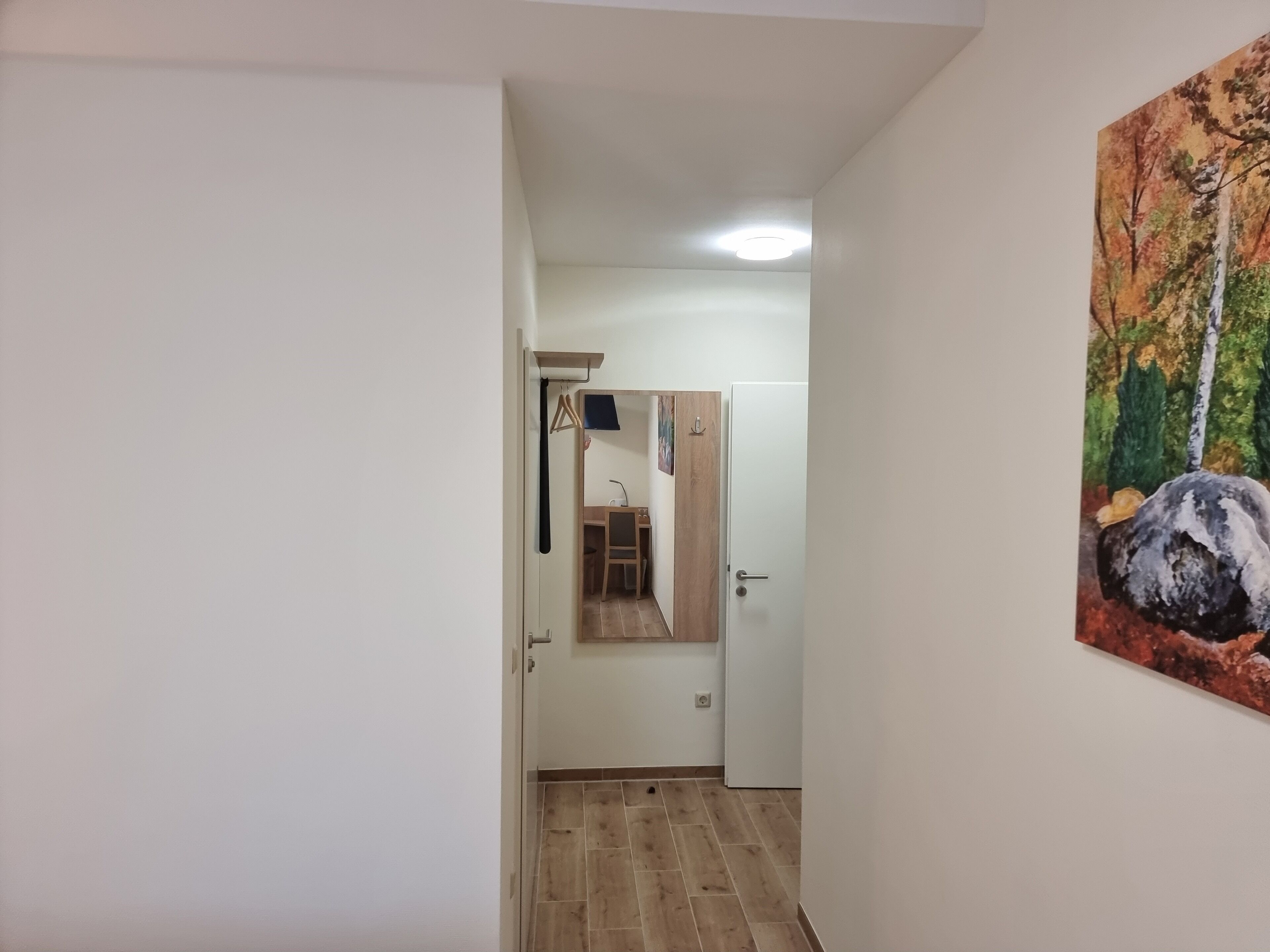 A hallway with a wooden floor, a white door, and a painting of a forest scene.