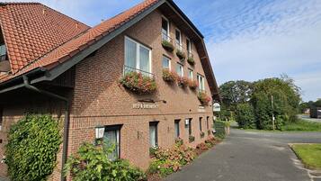 A brick building with a sign reading "BED & BREAKFAST" and "Grünewald." It has multiple windows with flower boxes and a paved driveway.