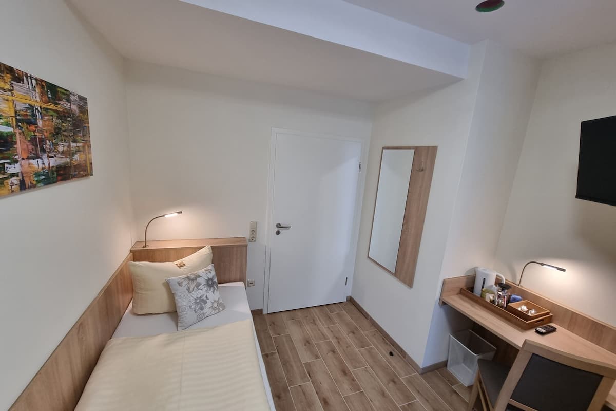 Quarto de hotel com cama, mesa de cabeceira, abajur e um espelho grande.