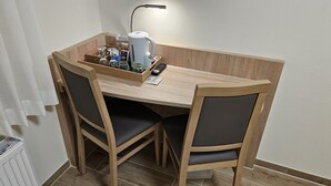 A small wooden dining table with two chairs, a kettle, a remote control, and a tray with glasses and condiments.