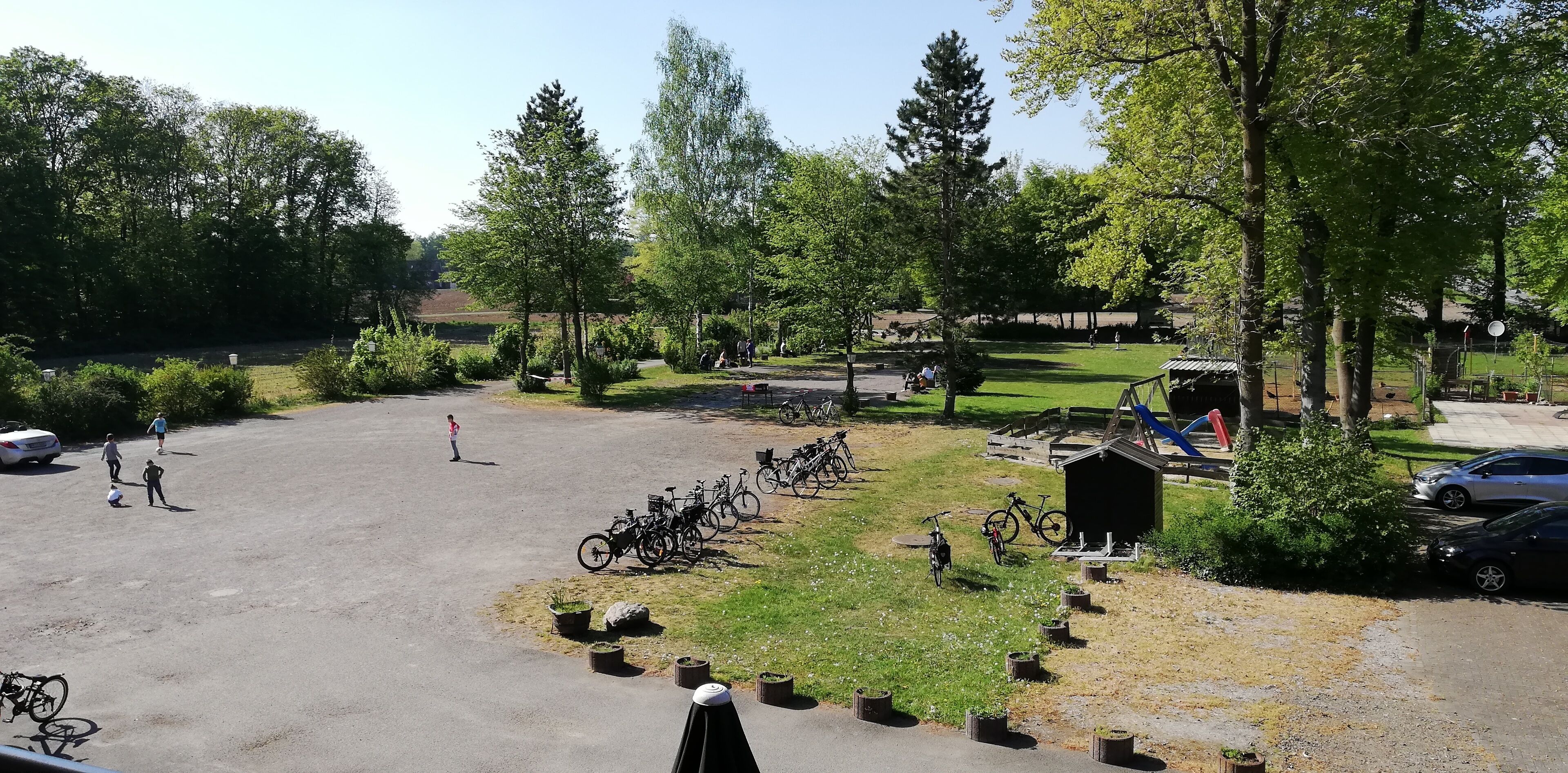 A parking lot with bicycles, a small shed, and a grassy area with trees.
