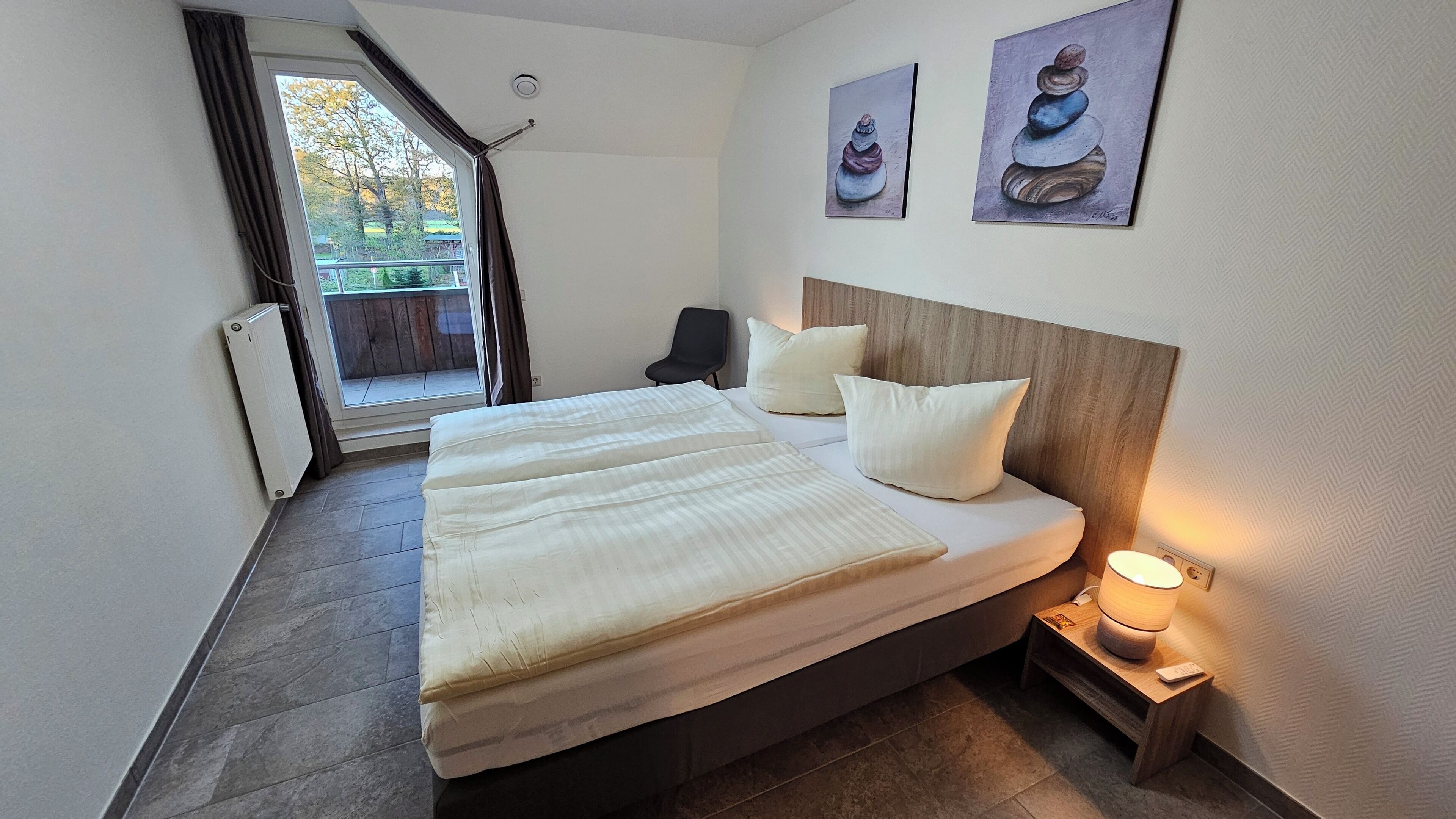 A hotel room with a bed, a chair, a nightstand, and a window with curtains.