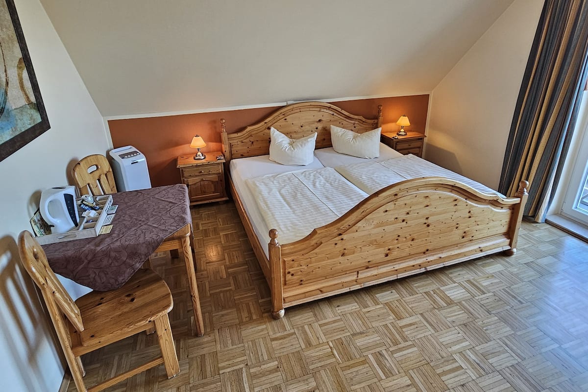 Quarto com cama de madeira, duas mesas de cabeceira com luminárias, escrivaninha de madeira com cadeira e piso em padrão herringbone.